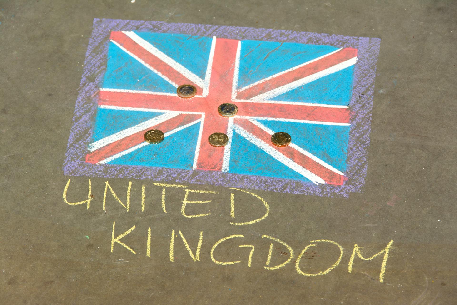 Colorful chalk drawing of the UK flag with coins on pavement, signifying currency and culture.