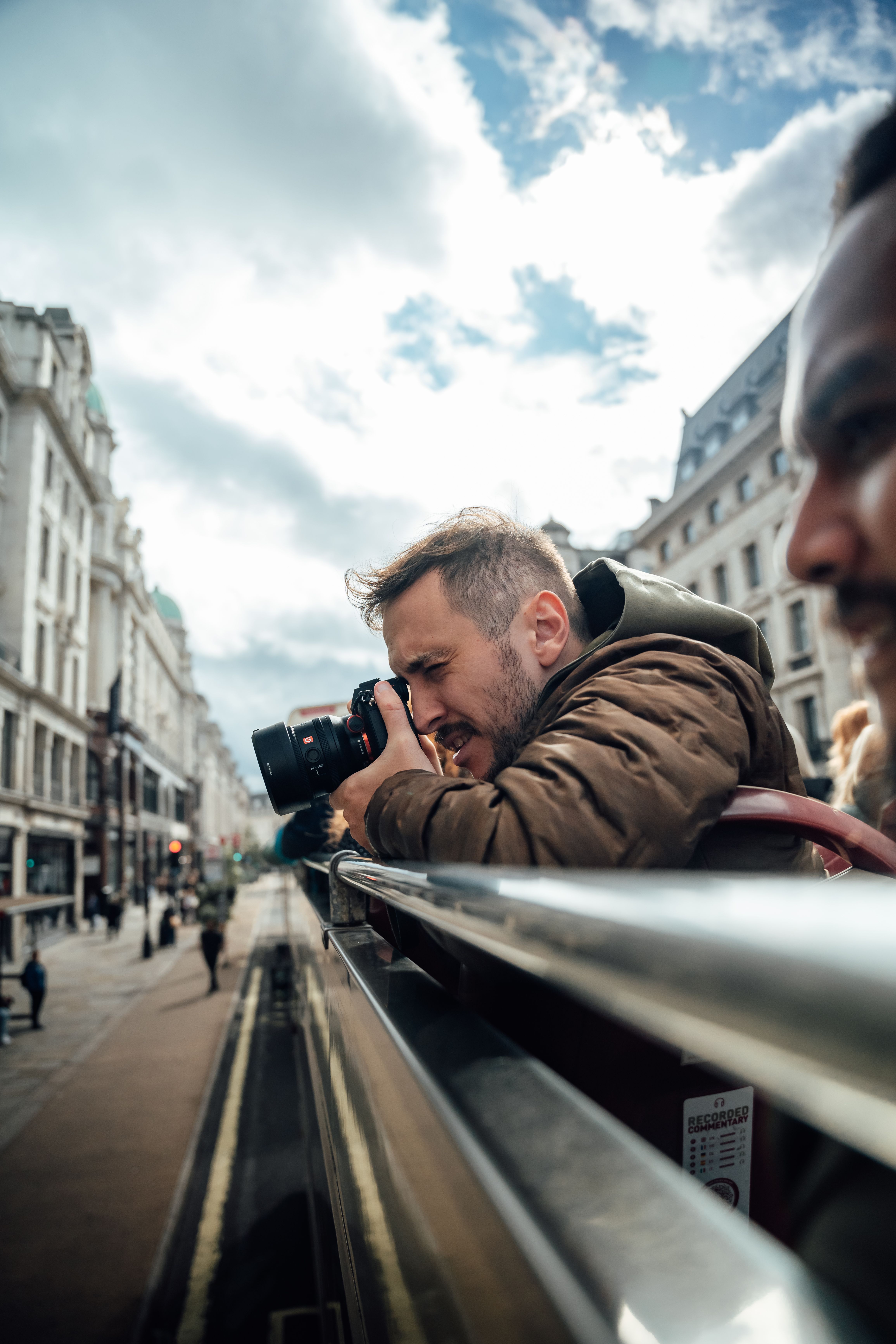 Man taking photos from an open-top bus in London, capturing city sights and street life.