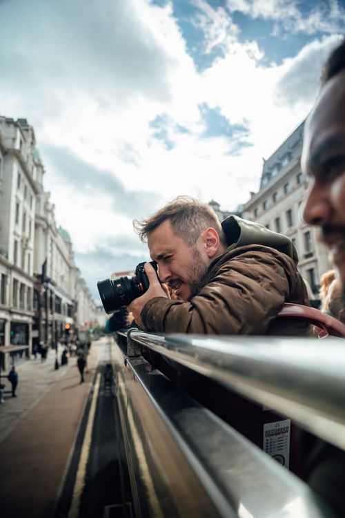 Free Man taking photos from an open-top bus in London, capturing city sights and street life. Stock Photo