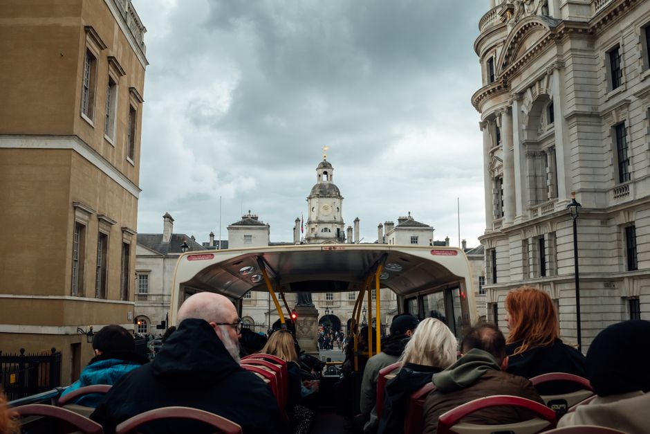 View from an open-top bus full of tourists in central London, showcasing historic architecture.