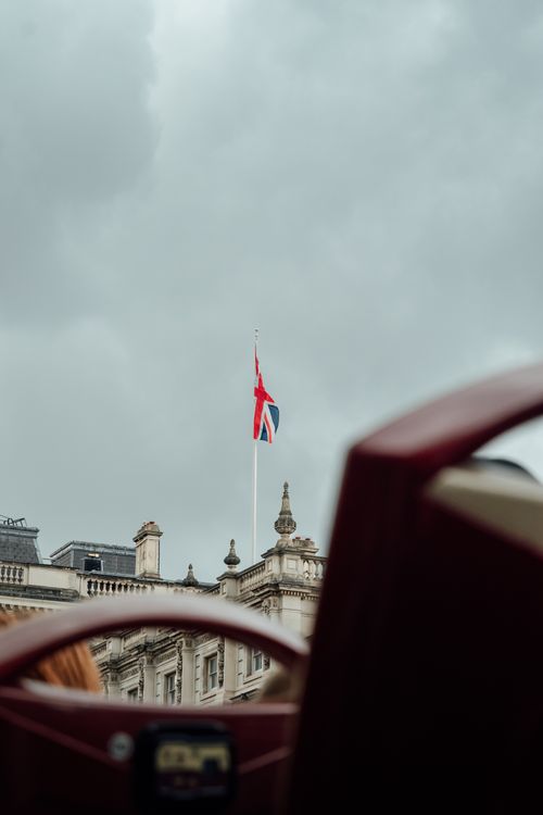 Free Union Jack flag flying over a historic London building under cloudy skies. Stock Photo