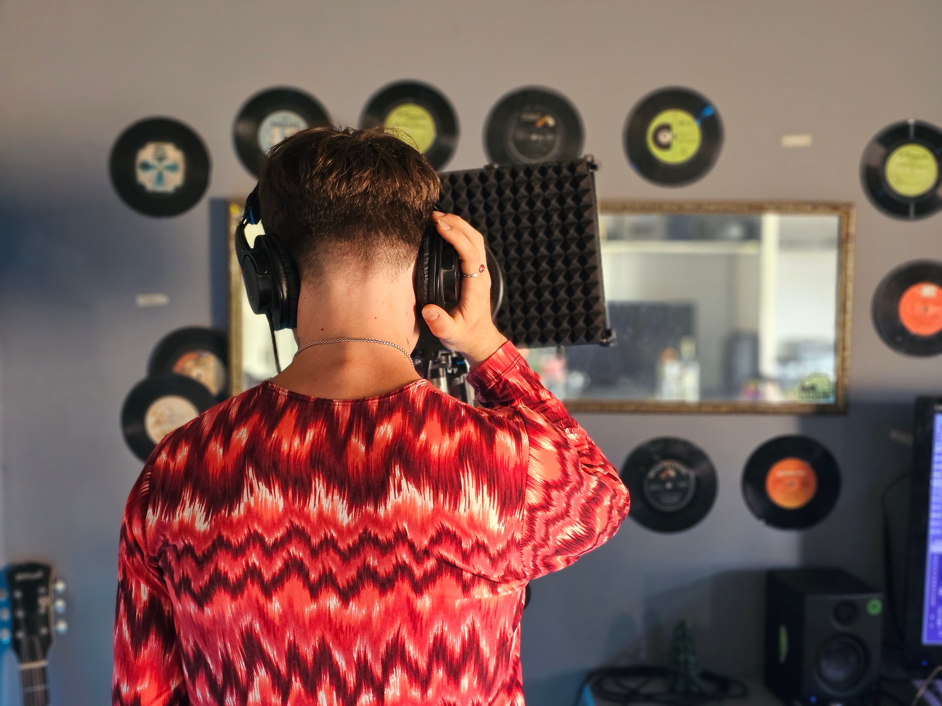 A musician in a studio looking at their phone, with a whiteboard behind them that says 
