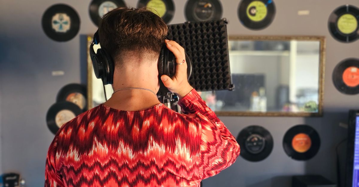 A musician in a studio looking at their phone, with a whiteboard behind them that says