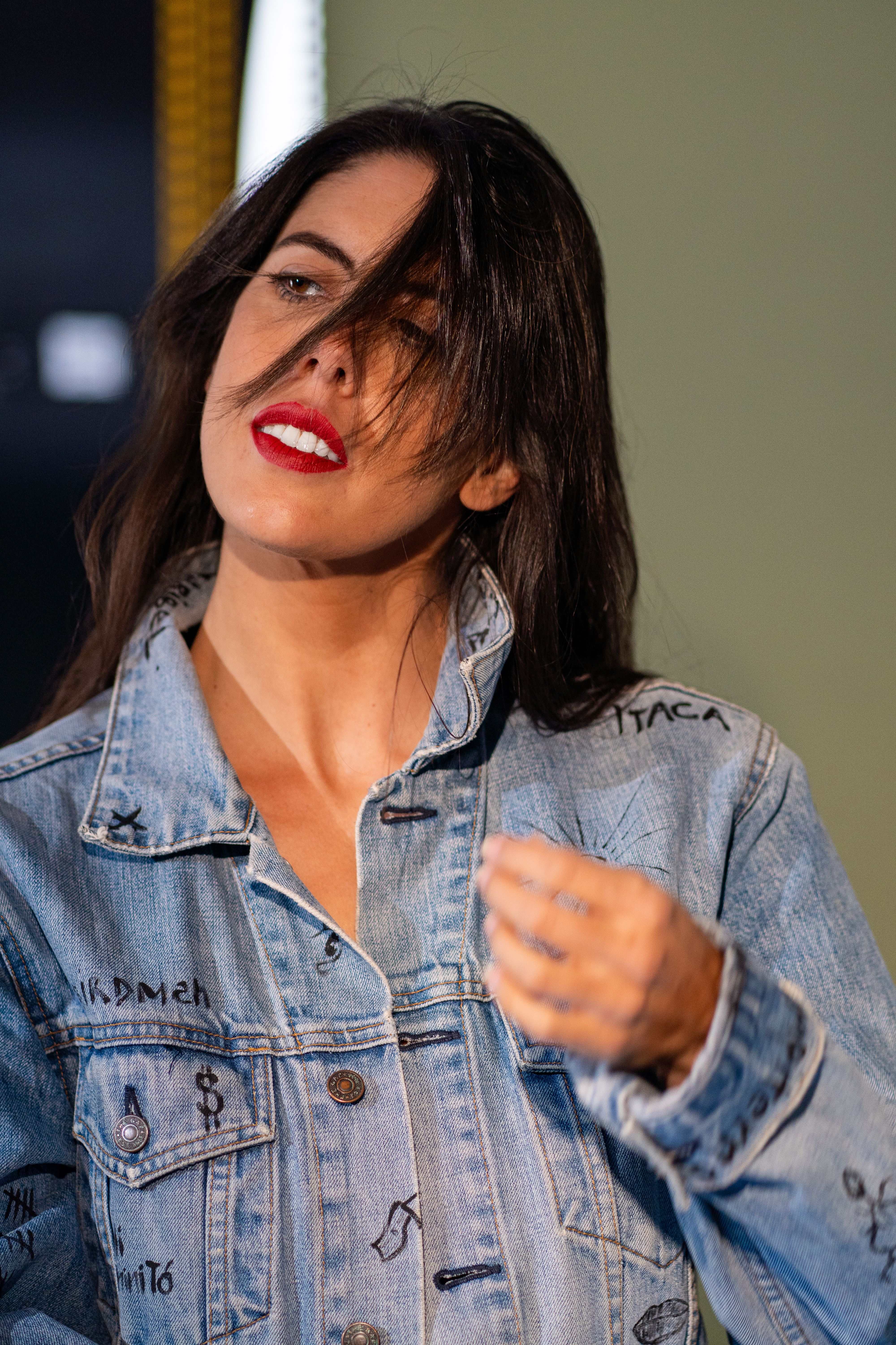 Confident woman with red lipstick and denim jacket in an indoor setting.