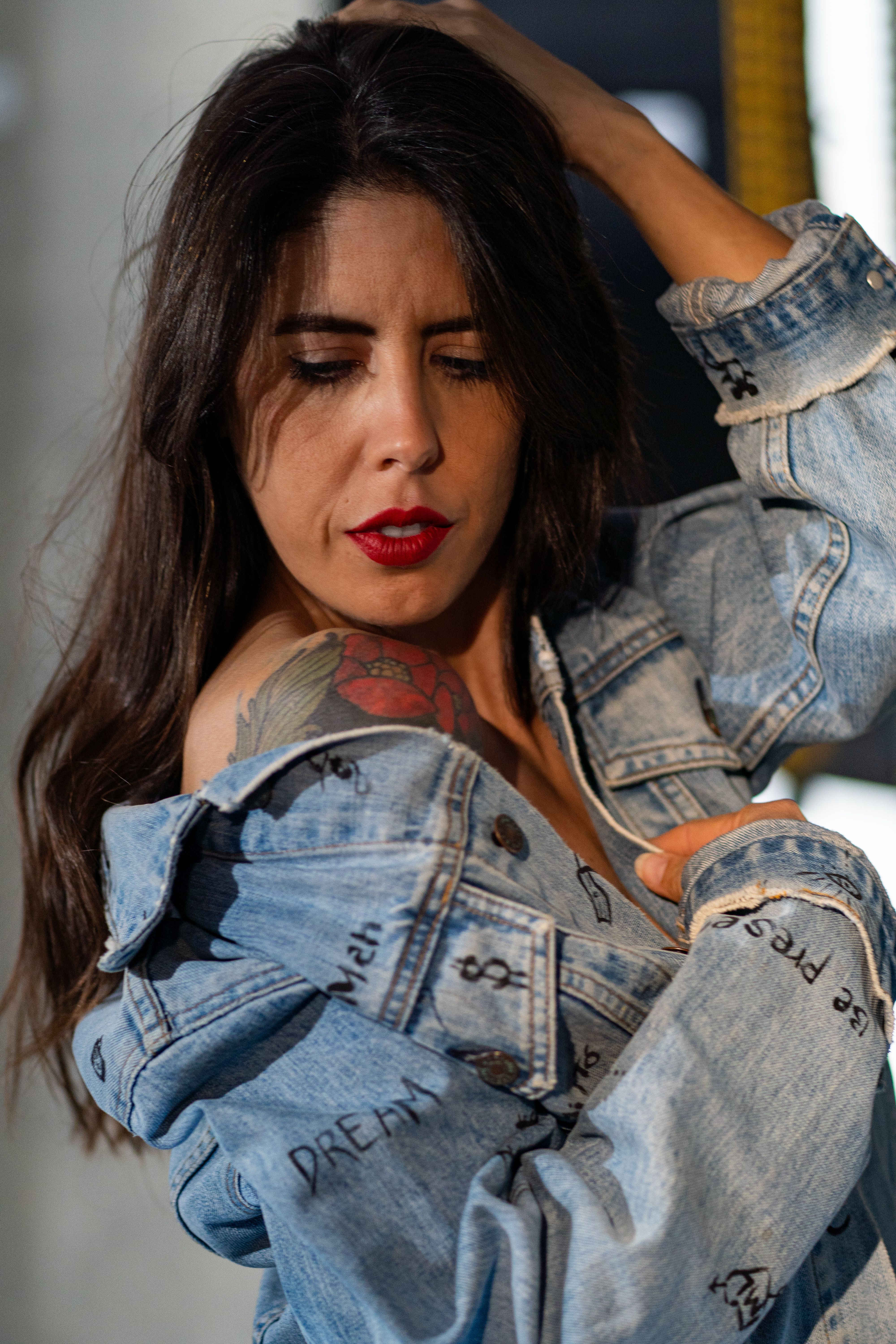 A fashionable woman poses confidently in a personalized denim jacket, showcasing tattoos.