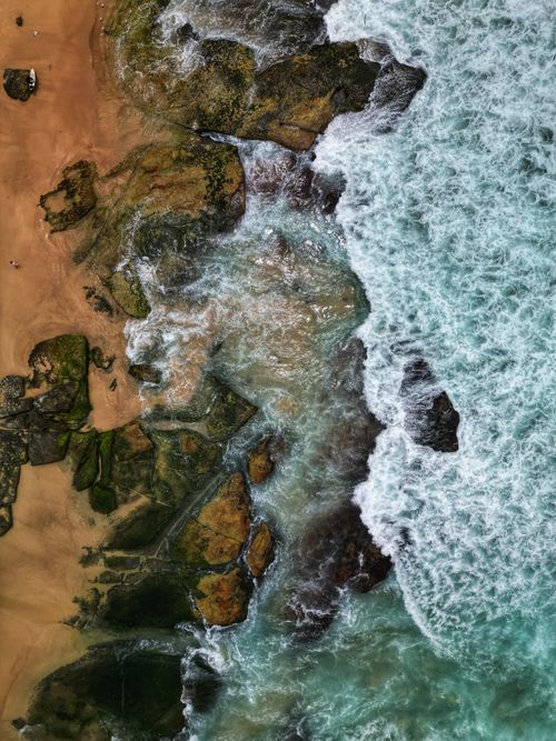 Free Stunning aerial view of ocean waves meeting a rugged rocky shoreline, showcasing nature's raw beauty. Stock Photo