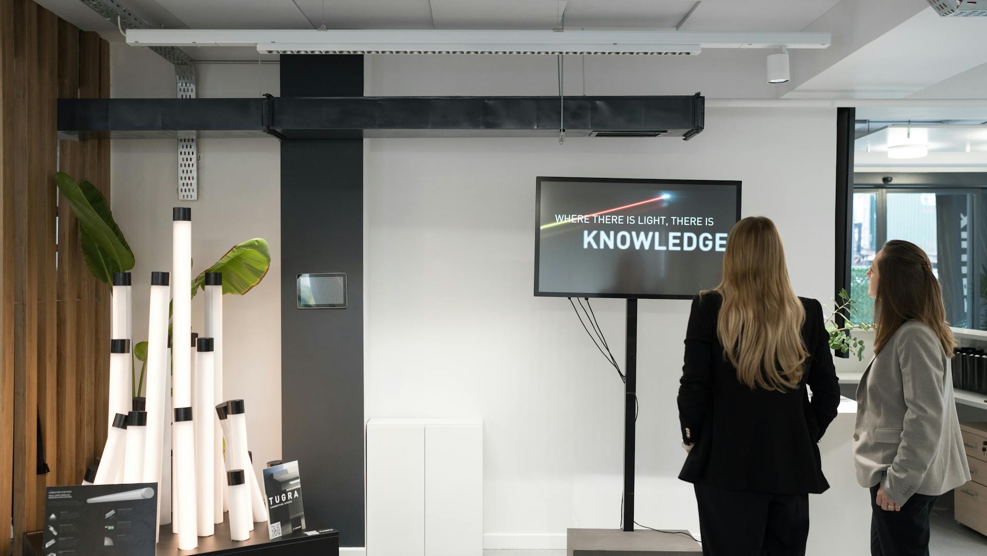 Two women in a modern office view a motivational quote on a screen inspiring knowledge.