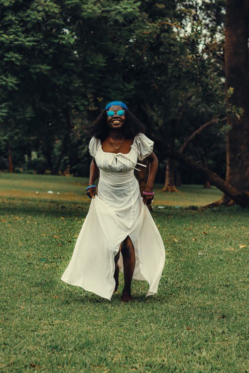 Free A joyful woman wearing a white dress and blue headband enjoying a sunny day in the park. Stock Photo
