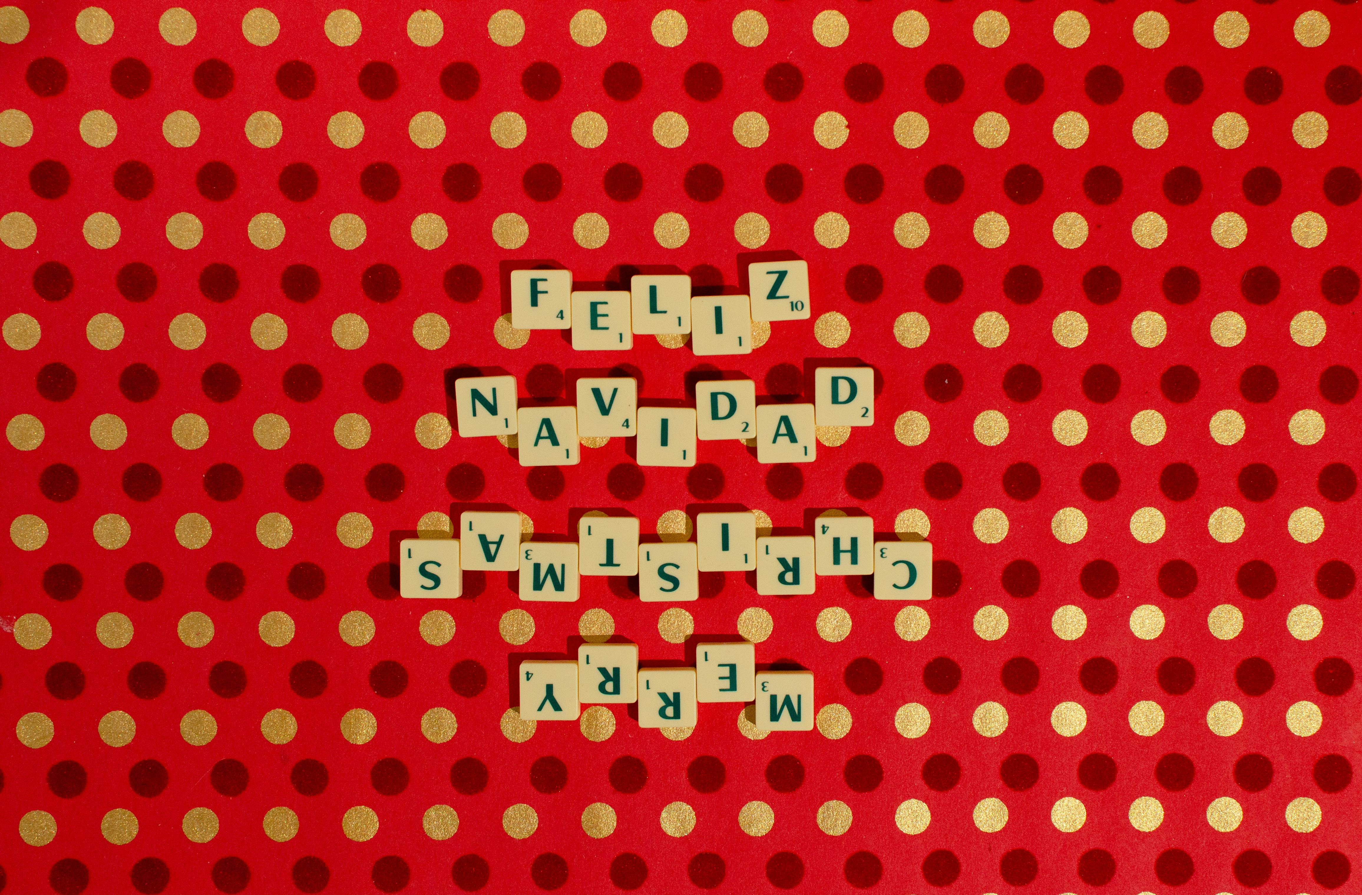 Gratis Scrabble-fliser som staver «god jul» og «Feliz Navidad» på et rødt prikkete bakteppe. Arkivbilde