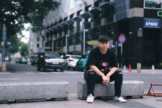 Casual urban street portrait of a young adult sitting on a bench in Hồ Chí Minh City's bustling district.