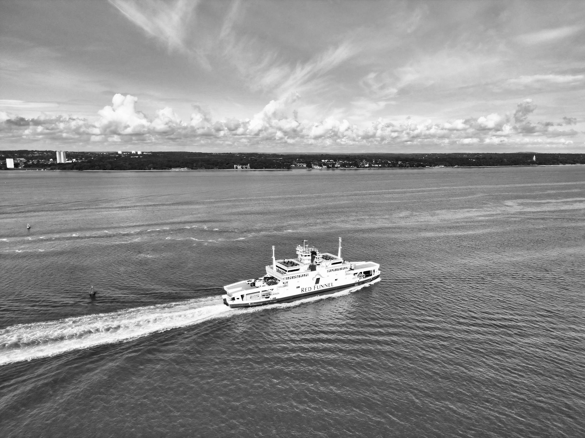 Black and white photo of Red Funnel ferry navigating the Solent with a coastal landscape in the background.