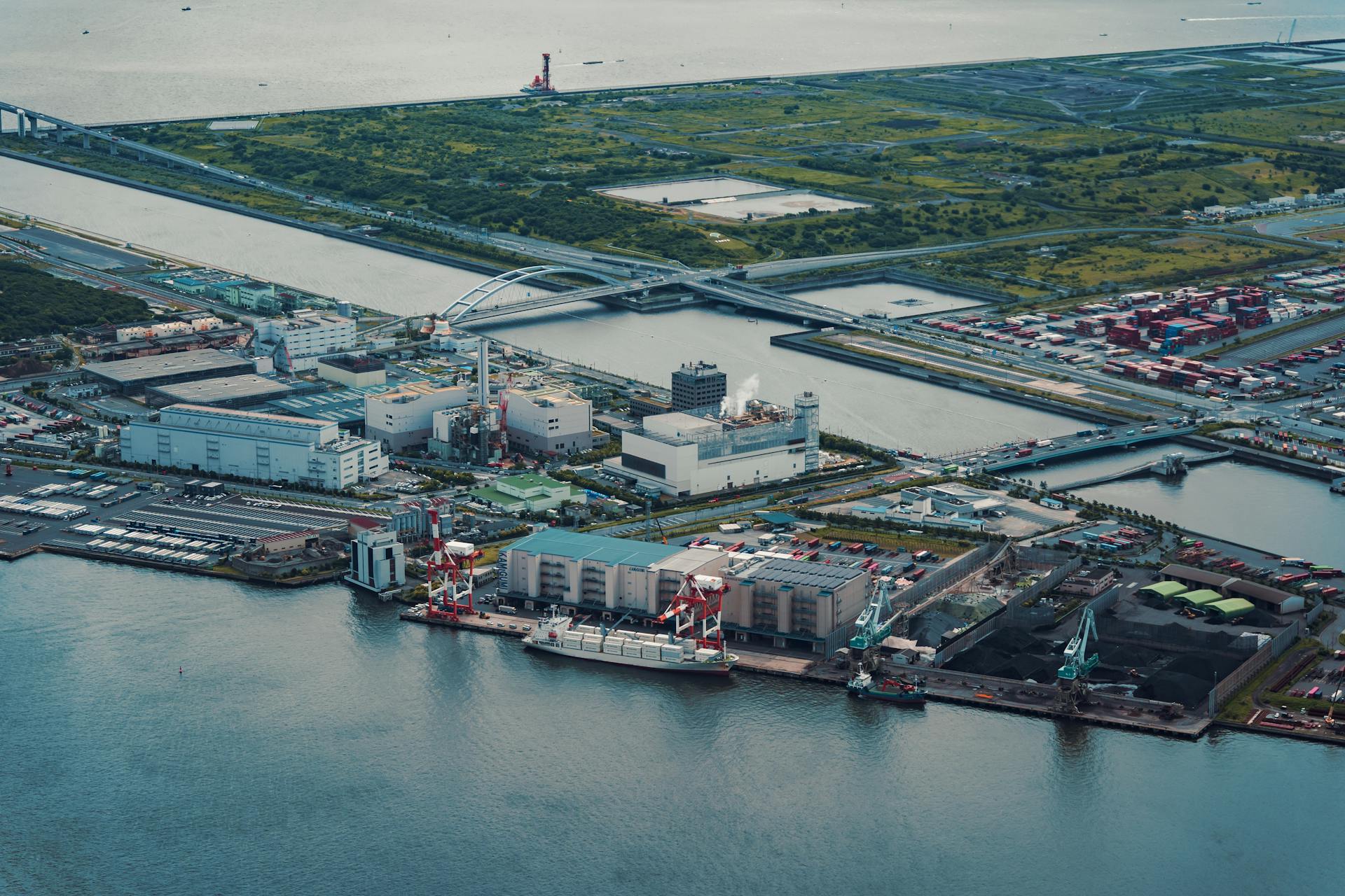 Aerial view of Tokyo's industrial port by the water, featuring cranes and containers.
