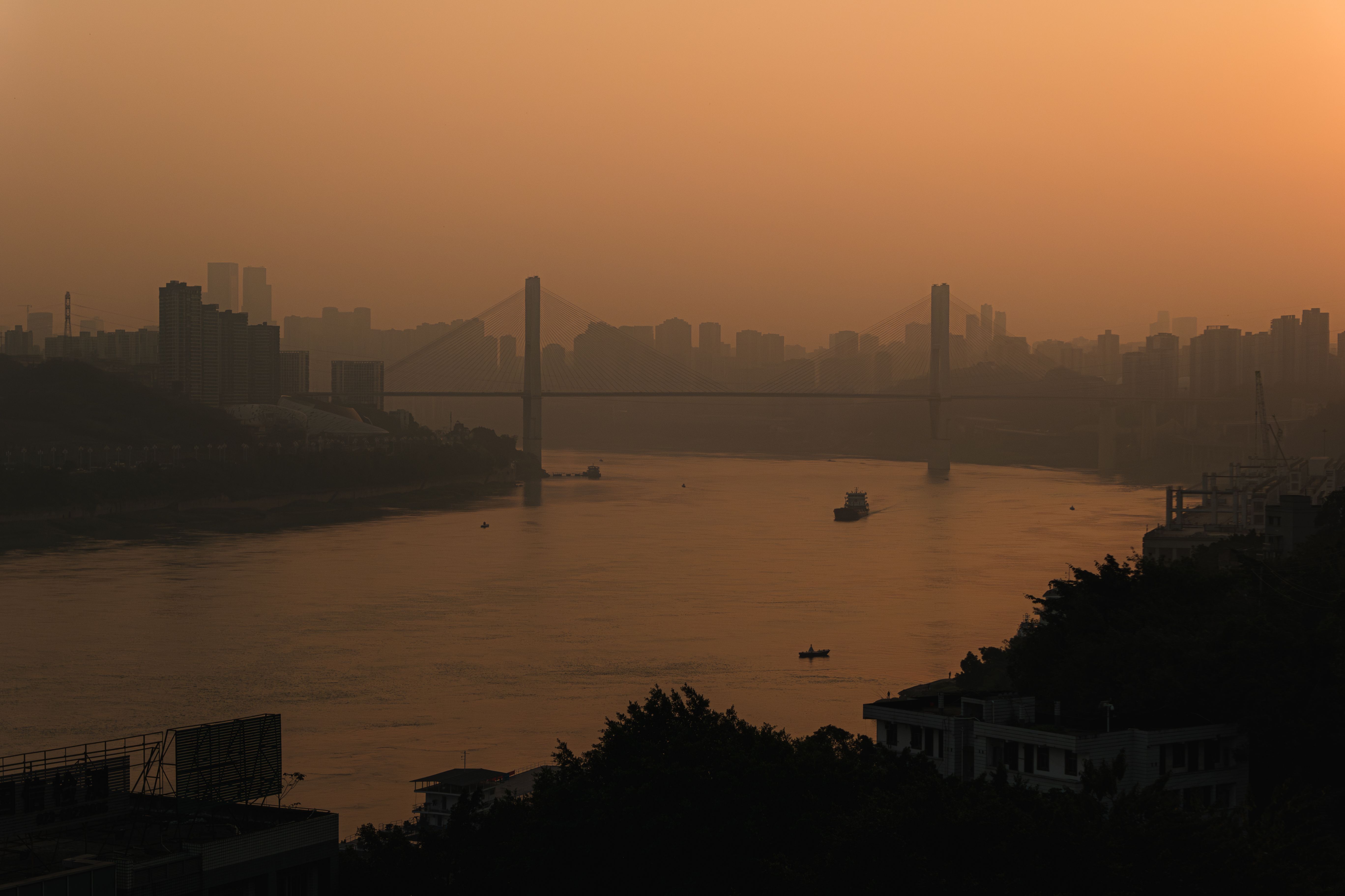 A city skyline and bridge silhouetted at sunset over a river