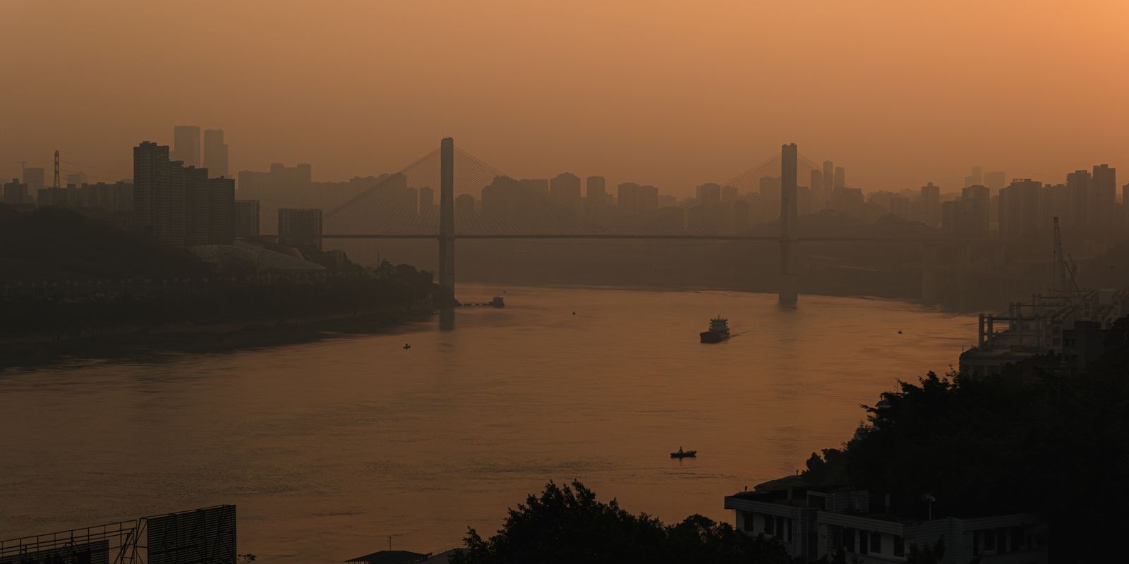 A city skyline and bridge silhouetted at sunset over a river