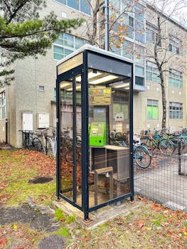 Glass phone booth outside building surrounded by bikes in autumn.