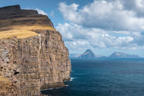 Free Stunning mossy cliffs meet the Atlantic Ocean under a dramatic sky in the Faroe Islands. Stock Photo