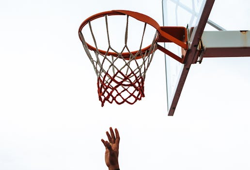 An upward view of a hand reaching for a basketball hoop on an outdoor court.