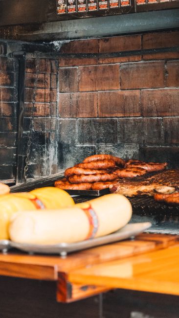 Fotomural Deliciosas salchichas y queso a la parrilla sobre una mesa de madera en un ambiente rústico de ahumadero.