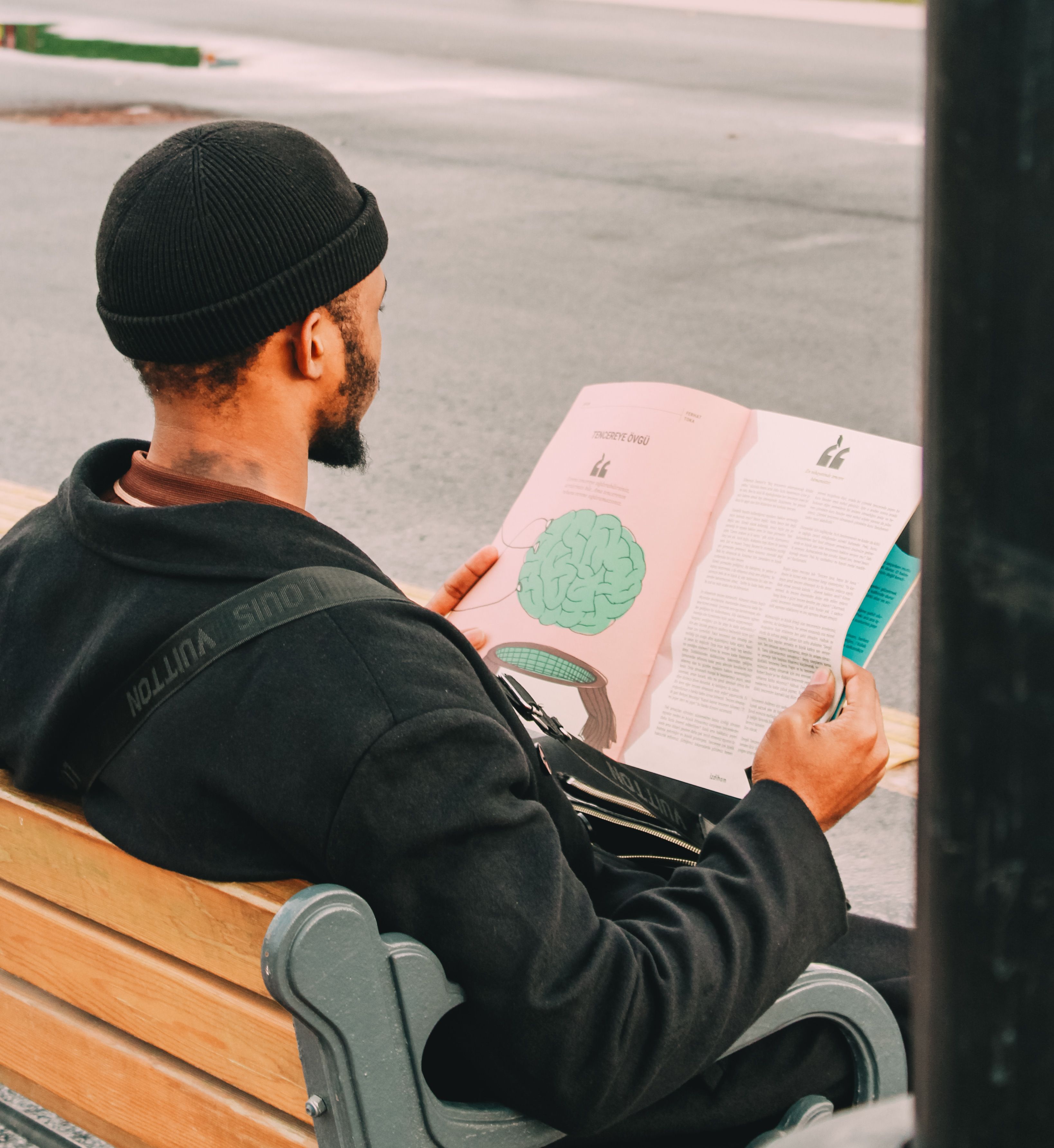 A man casually reads a magazine on a park bench, enjoying a relaxing moment outdoors.