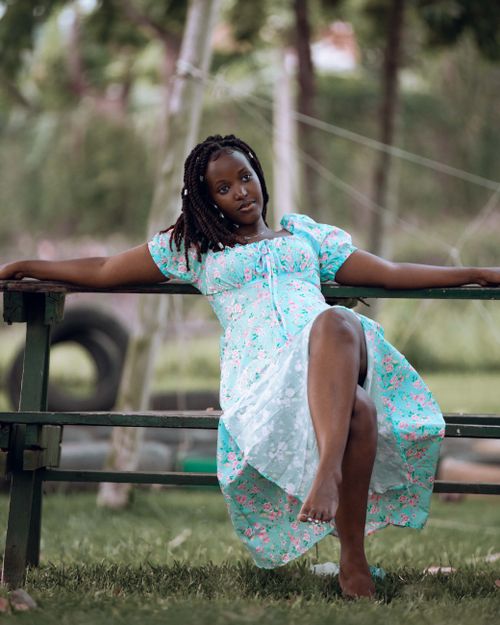 Free A woman in a floral dress with dreadlocks sitting casually outdoors on a wooden bench. Stock Photo