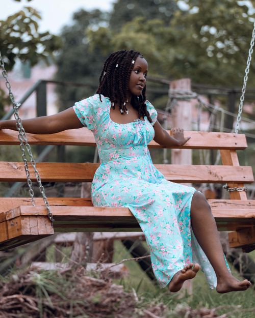 Free A woman in a floral dress relaxing on a wooden swing outdoors, surrounded by nature. Stock Photo