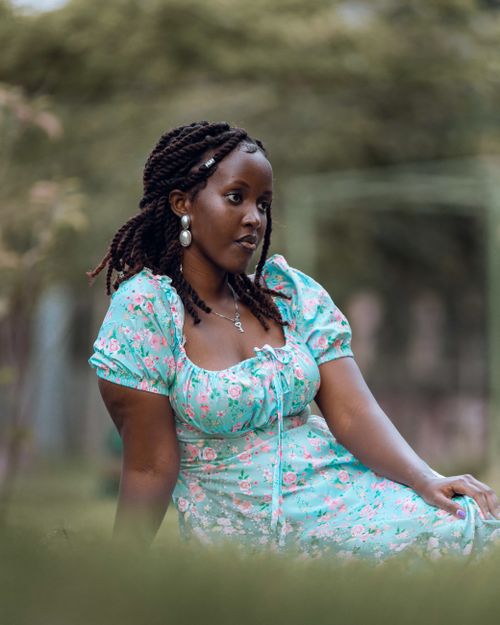 Free A young woman wearing a floral dress lounges in an outdoor garden. Stock Photo