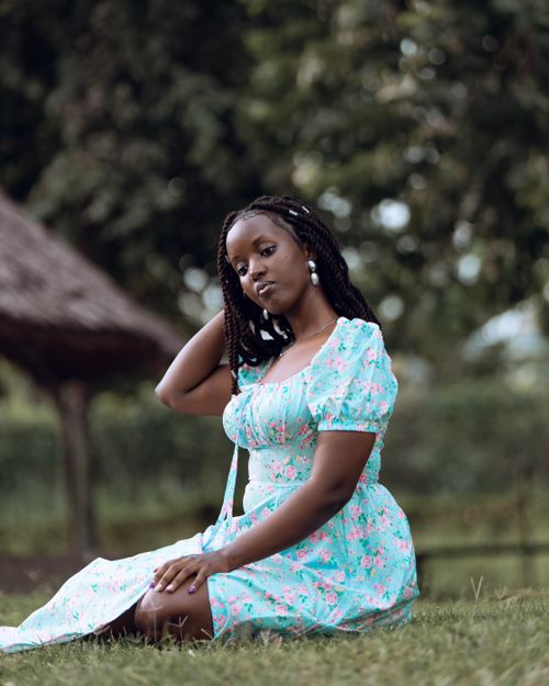 Free Young woman in a floral dress sitting on grass in a natural setting, relaxed pose. Stock Photo