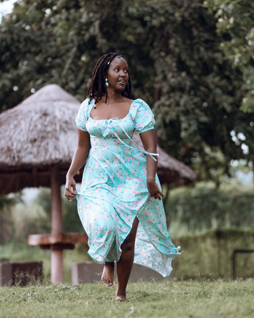 Free Young woman in a floral dress joyfully walking in a lush outdoor setting. Stock Photo