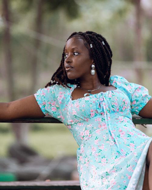 Free A woman in a floral dress relaxes on a park bench, enjoying a peaceful moment outdoors. Stock Photo