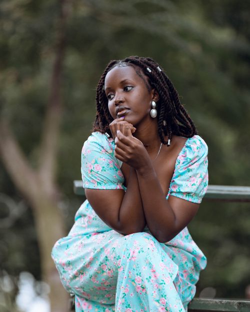 Free A woman in a floral dress sits thoughtfully on a bench in a natural setting. Stock Photo