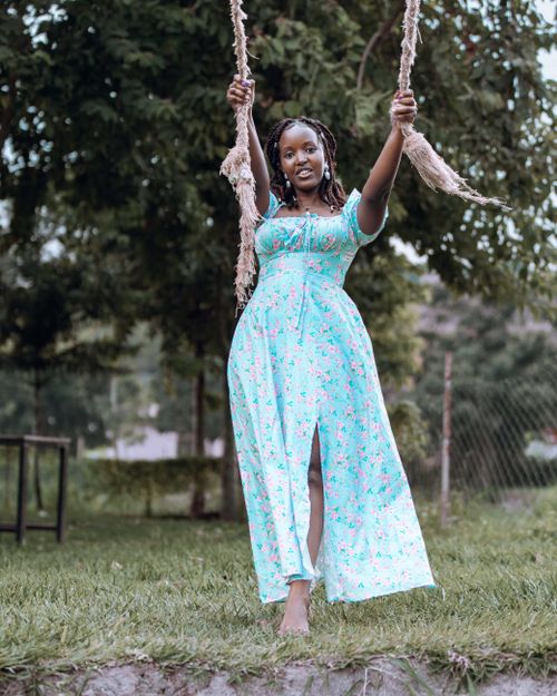 Free A cheerful woman in a floral dress enjoys swinging in a lush outdoor setting. Stock Photo