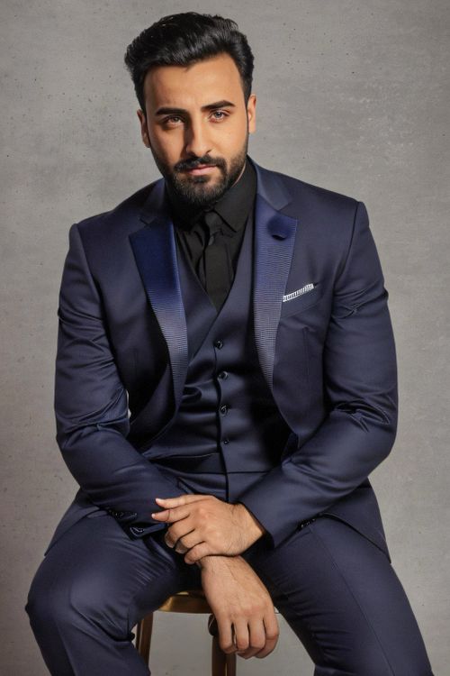 Free Handsome man in a navy suit sitting elegantly indoors with a confident look. Stock Photo