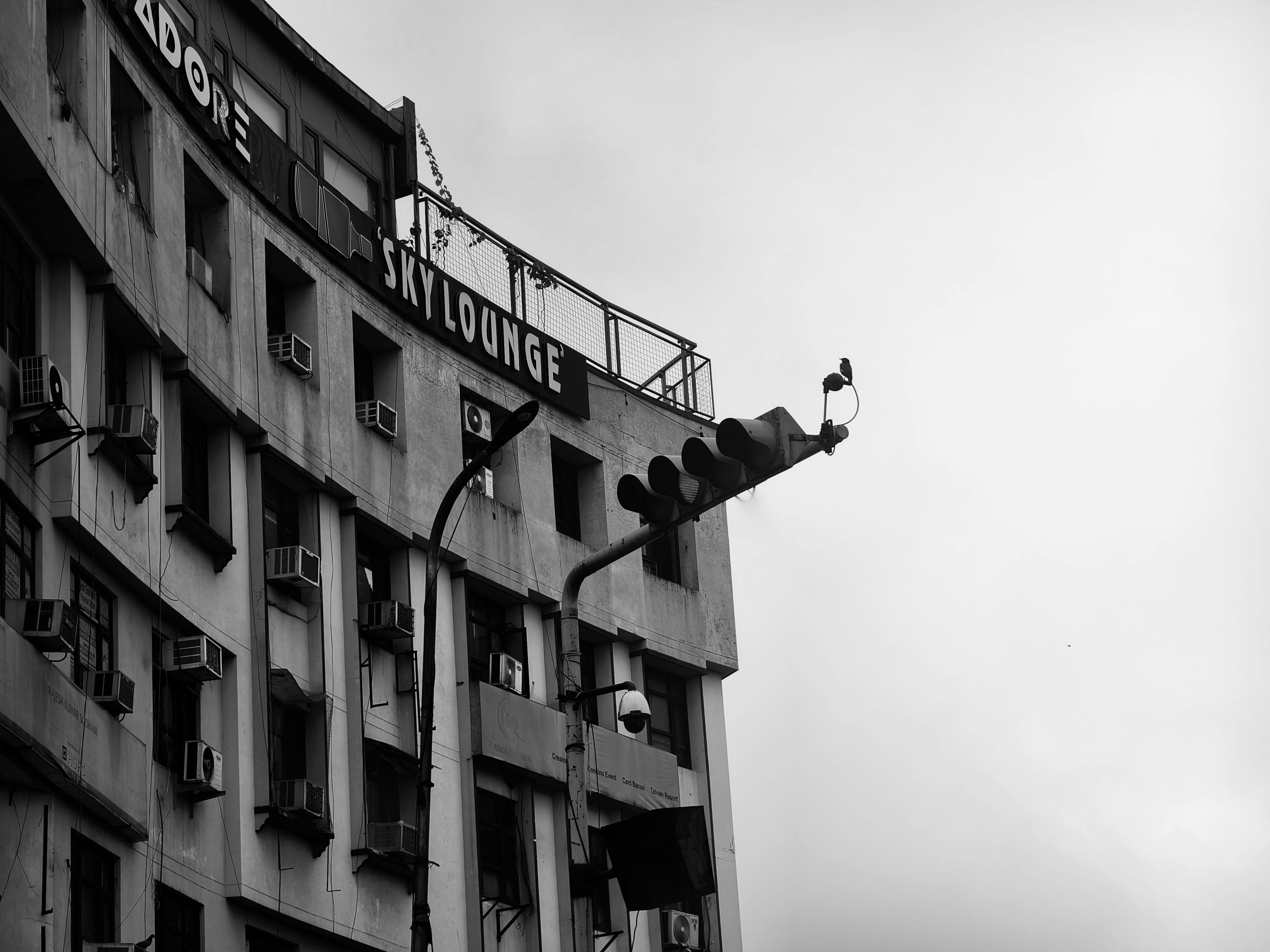 Gratuit Photo en noir et blanc d'un bâtiment de la ville avec un panneau sur le toit et un feu de circulation. Photos