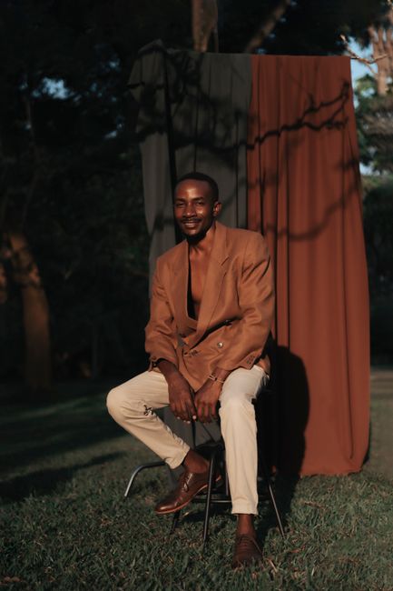 Portrait of a stylish man in a blazer sitting outdoors with dramatic shadows.
