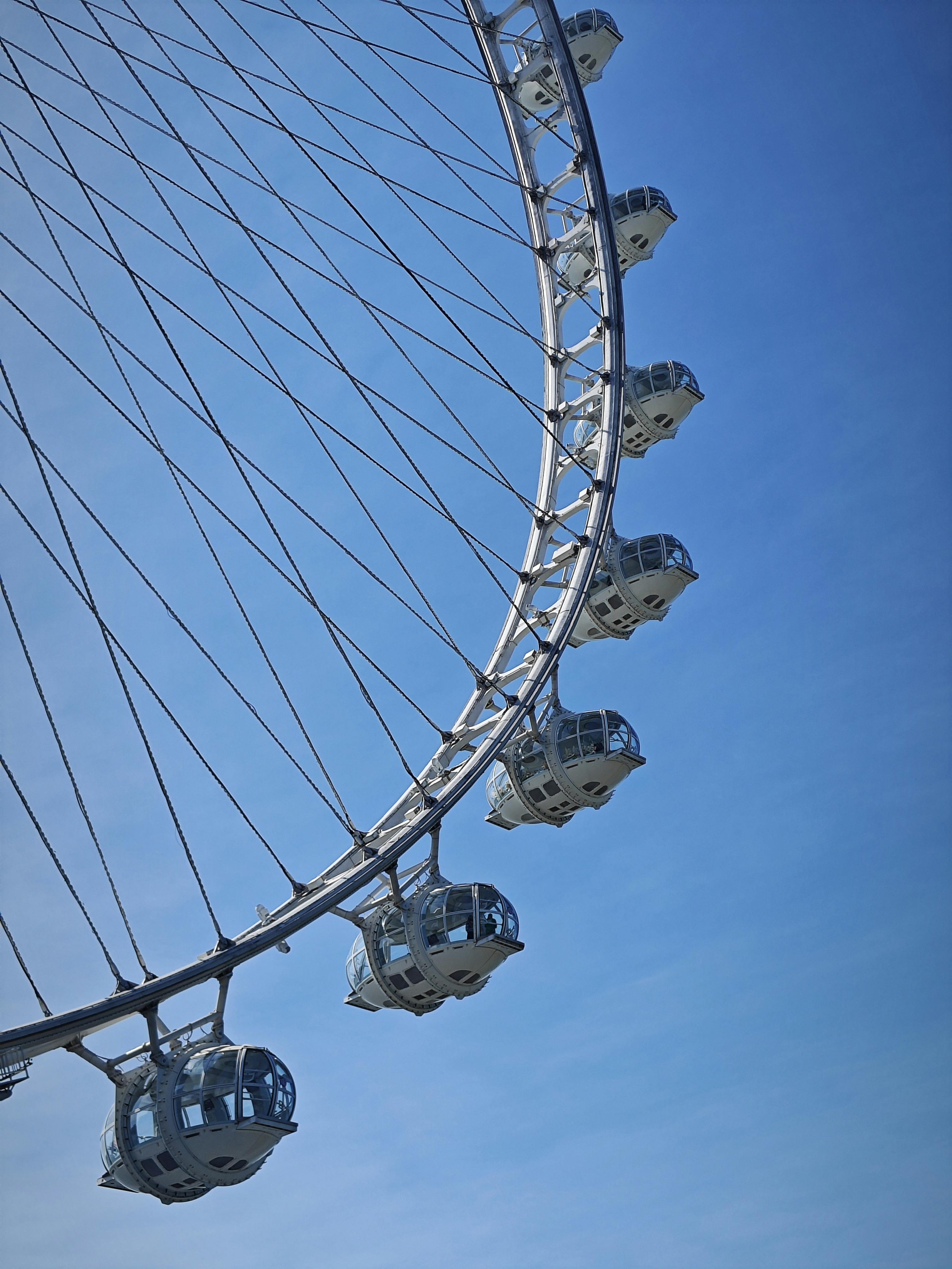 Close-up of a Ferris wheel with cabins against a clear blue sky, capturing urban leisure.