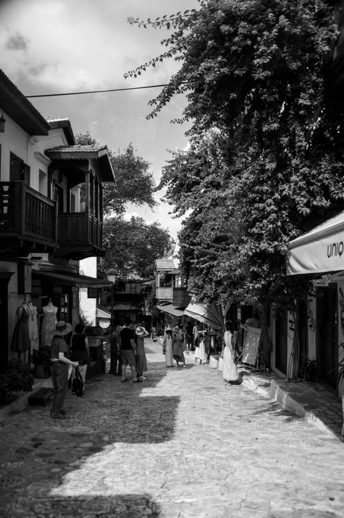 Free Black and white image of a bustling cobblestone street market with people shopping under shade. Stock Photo
