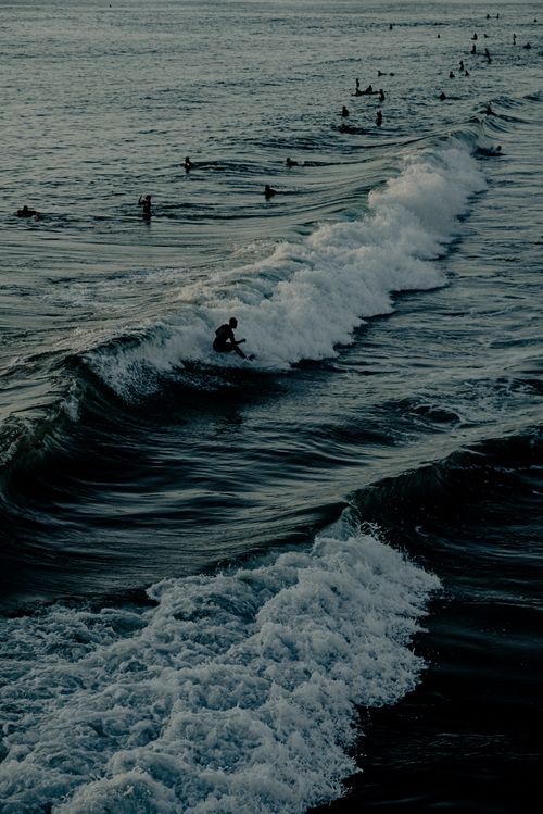 Free Silhouetted surfers ride waves at sunset, creating a dynamic ocean scene. Stock Photo