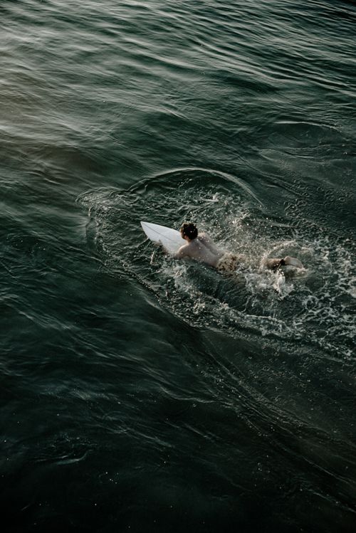 Free A surfer paddles through the ocean waves during a late afternoon with a serene ambiance. Stock Photo