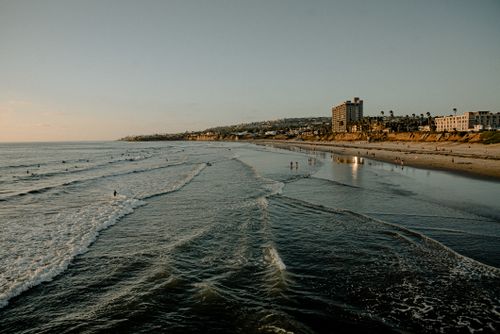 Free Scenic beach view with waves and buildings during sunset, offering a tranquil coastal atmosphere. Stock Photo