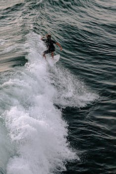 A surfer skillfully rides a wave in the ocean during sunset, showcasing adventure and exhilaration.
