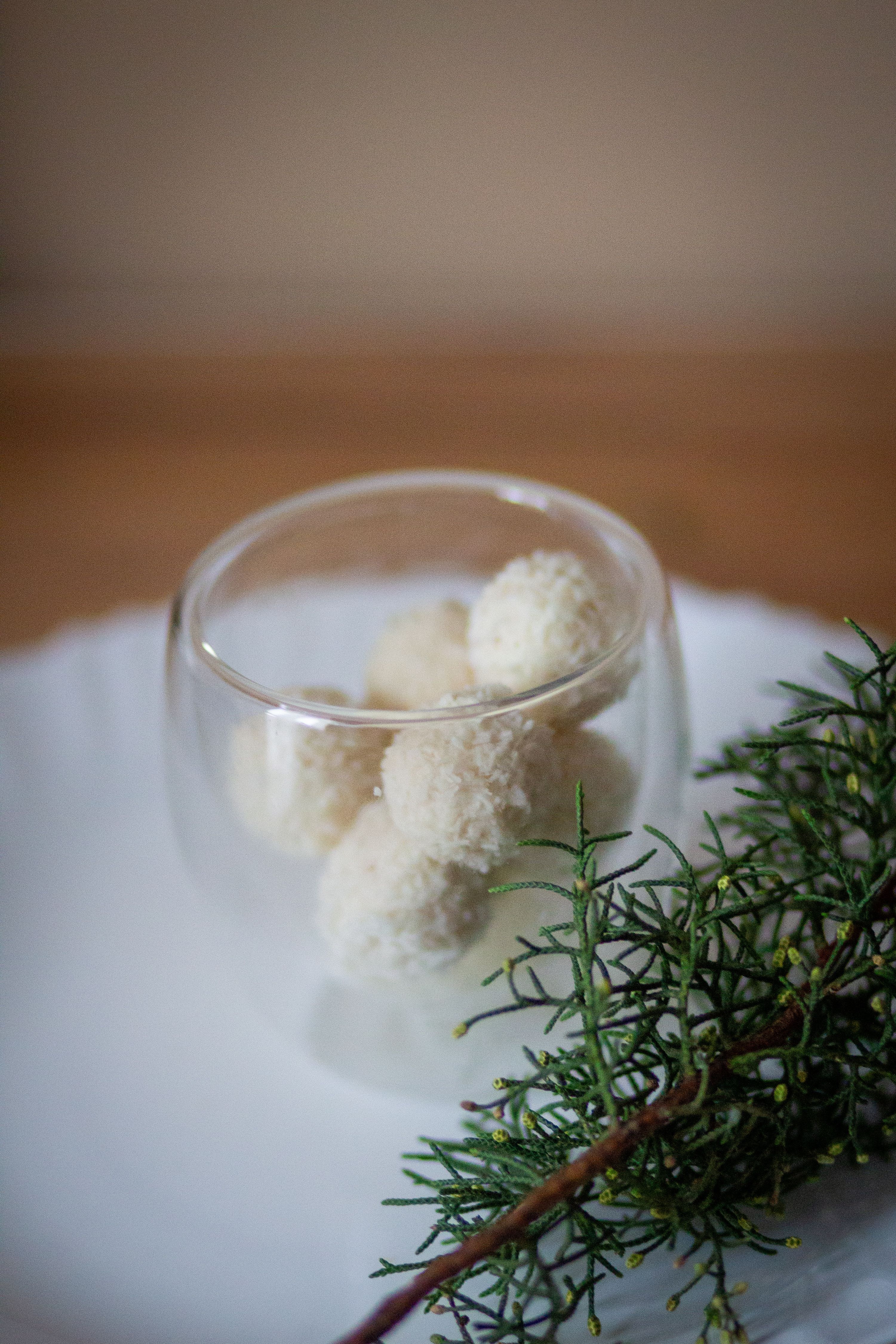 Simple elegance with white truffles in glass bowl, accented by evergreen branch.