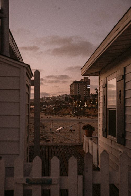 Free Seaside view between houses showcasing a beach and distant hotel at sunset. Stock Photo