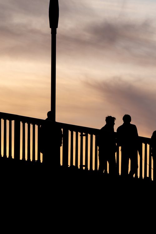 Free Silhouetted figures on a bridge against a vibrant sunset sky, capturing a moody and artistic scene. Stock Photo