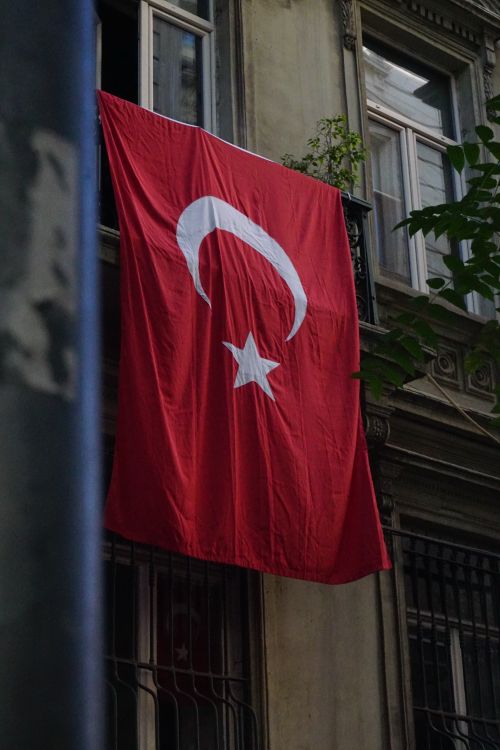 Free Turkish flag hung from an old building window in Istanbul, showcasing national pride. Stock Photo
