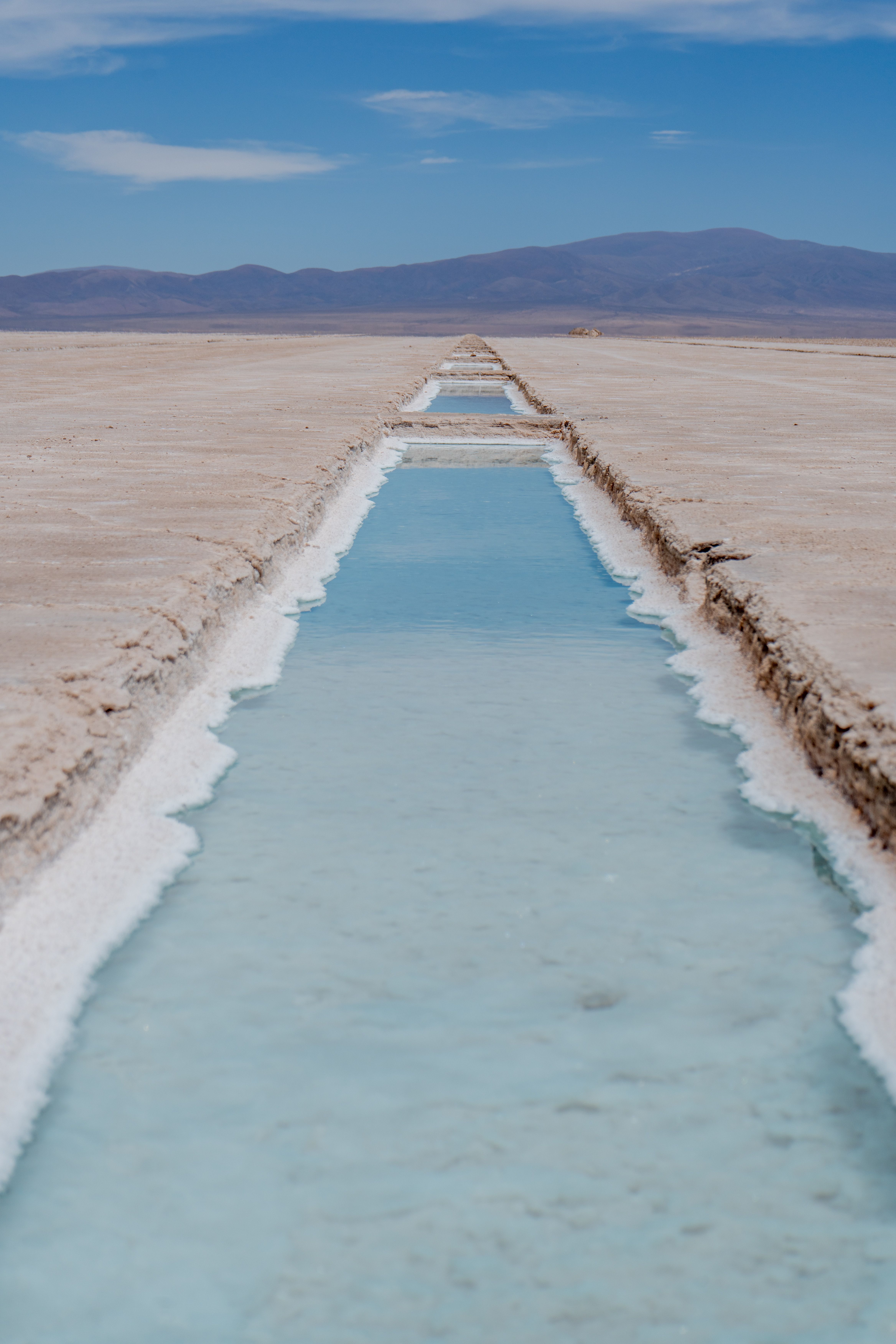 Canal de salmuera turquesa abierto en la costra de sal, con cerros al fondo
