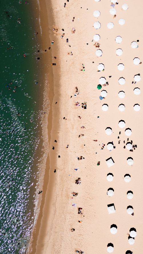 Free Aerial snapshot capturing a vibrant beach scene with umbrellas and ocean waves. Stock Photo