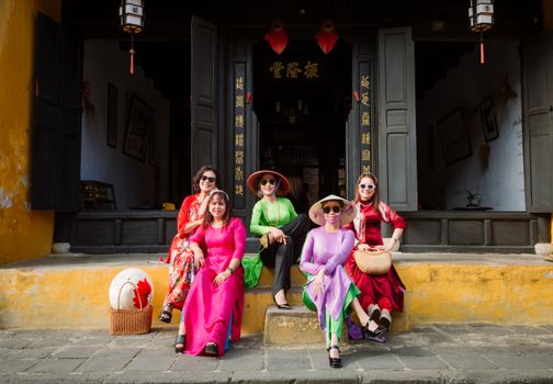 Group of women wearing Ao Dai sitting outside a historic building in Hội An, Vietnam.