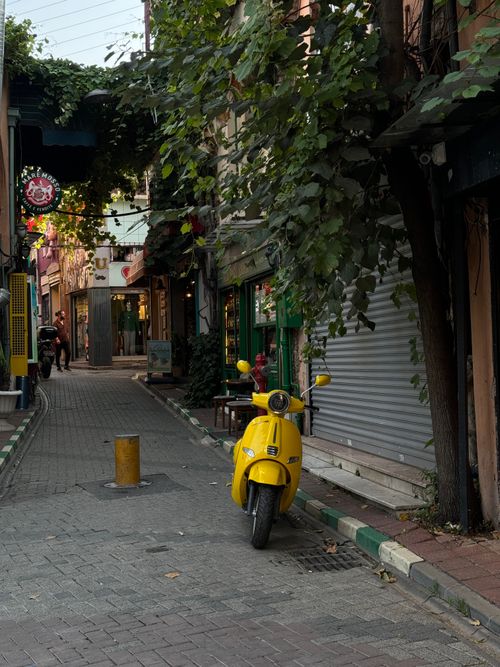 Free Cozy alley featuring a yellow scooter and charming architecture under leafy trees, ideal for lifestyle imagery. Stock Photo