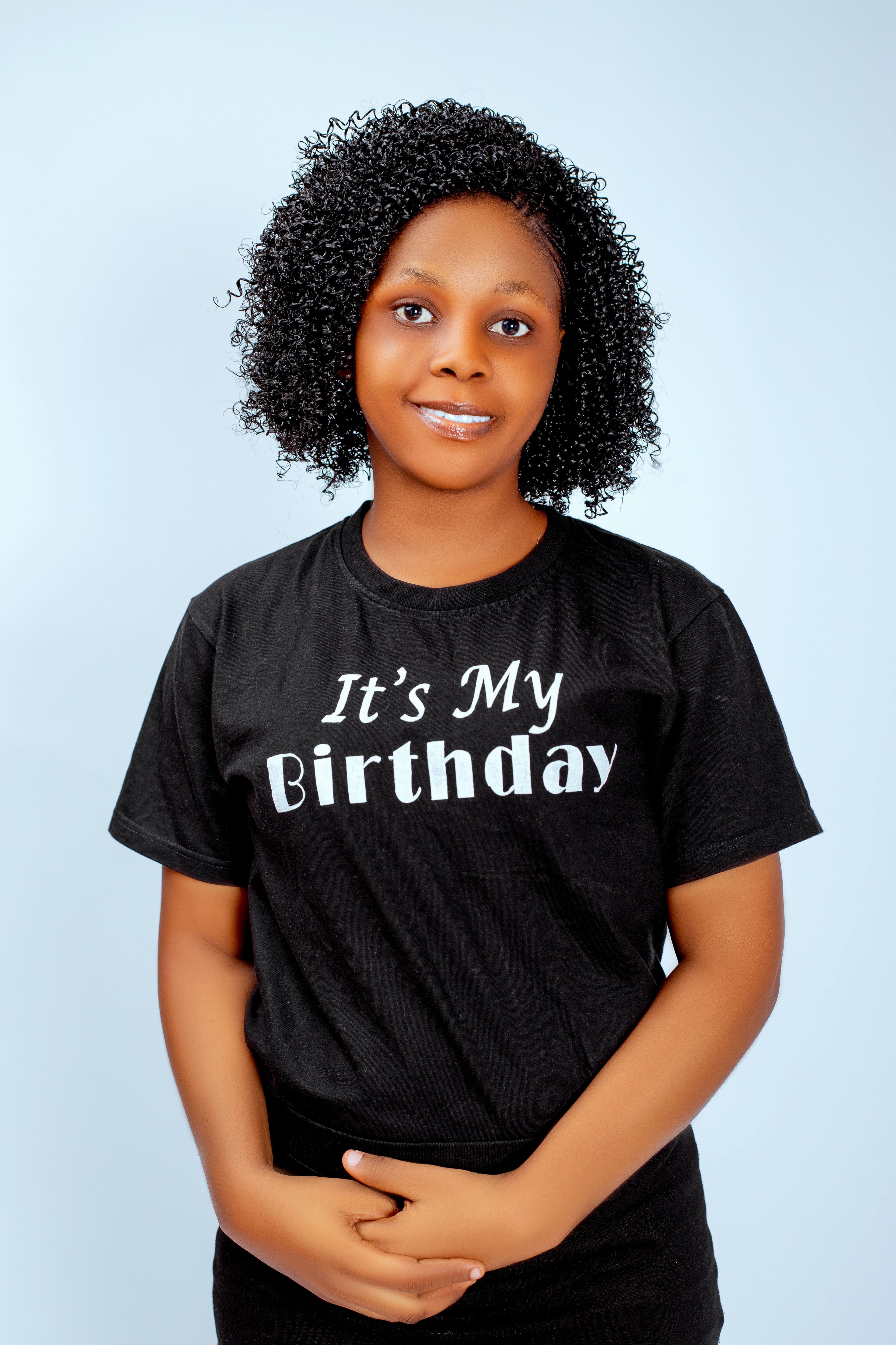 A woman in a black T-shirt with 'It's My Birthday' printed on it, smiling indoors.