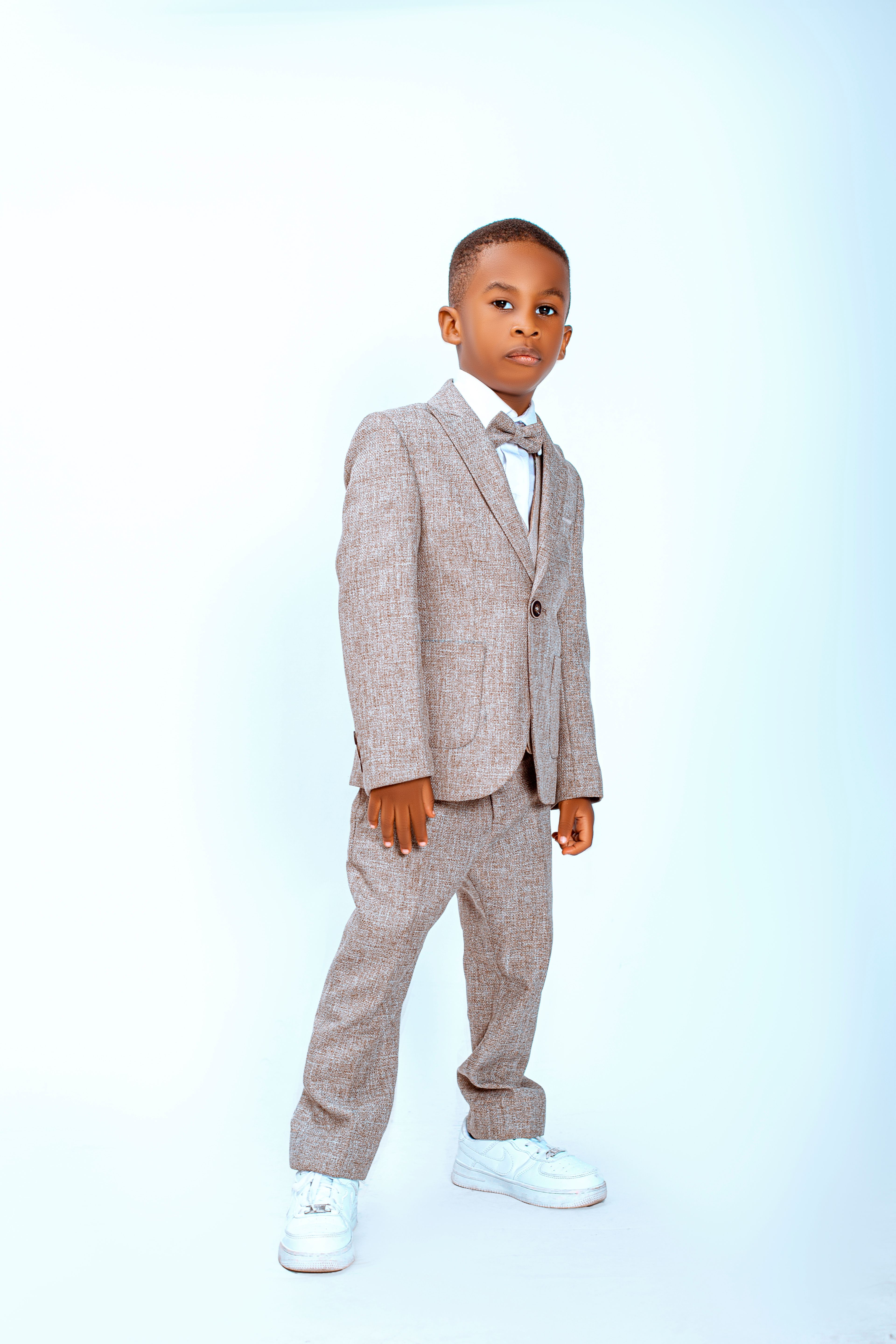 Charming young boy in a grey suit standing confidently on a white background.